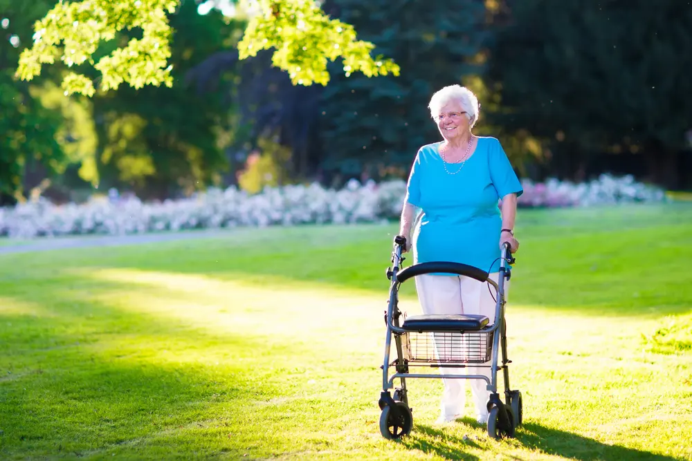 Older woman walking outdoors with a four-wheel rollator